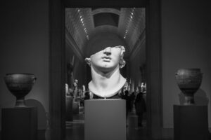 Marmeren buste belicht in een donkere museumzaal met urnen