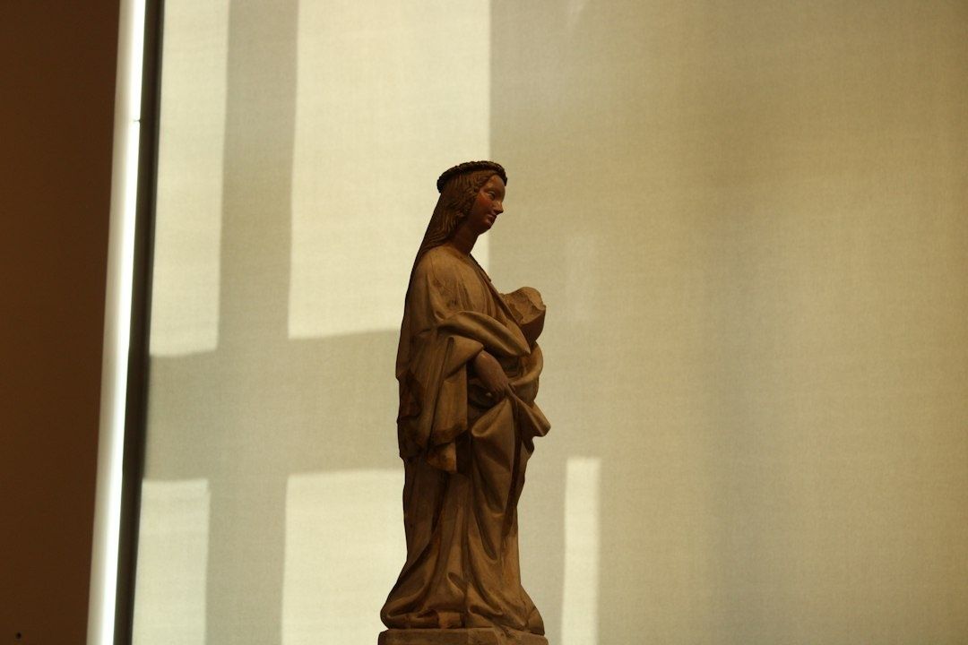 Houten beeld van een staande vrouw in warme, dramatische museumverlichting